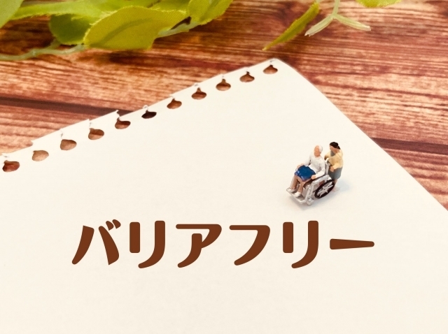 バリアフリーのイメージ。白い紙にバリアフリーのロゴ。車椅子介助している人形。